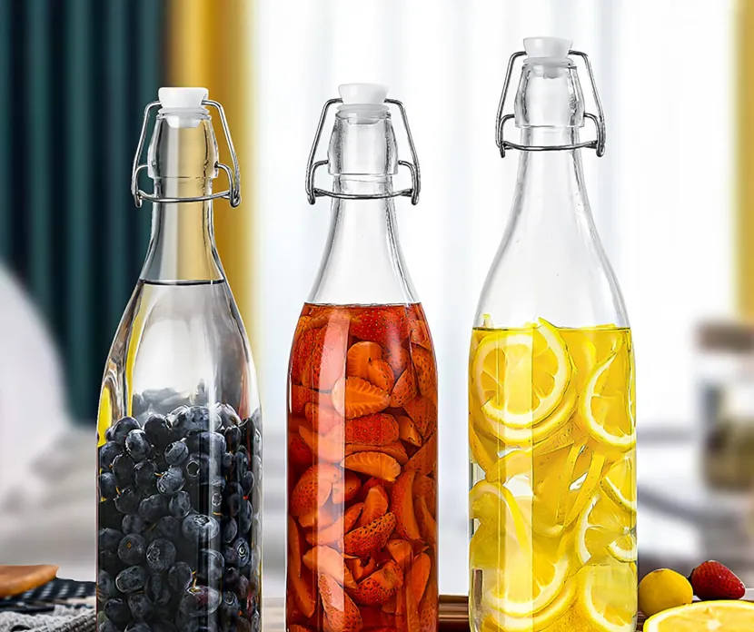 Three glass bottles with swing-top lids are filled with fruit-infused water, displayed on a wooden surface.